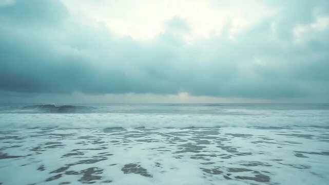Gentle ocean waves rolling onto a quiet sandy shore under a moody overcast sky, foamy surf tracing patterns along the empty coastline, calm and reflective seascape