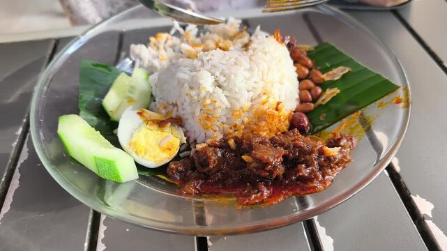 Fragrant nasi lemak is served on a glass plate with a fried egg. It comes complete with spicy sambal, crunchy peanuts, and fresh cucumber slices. This iconic Malaysian dish is ready to enjoy.