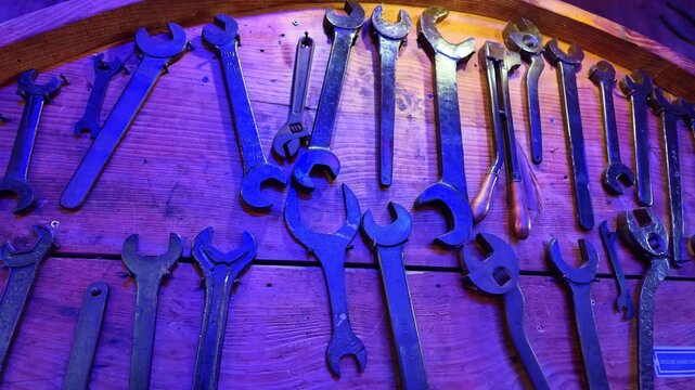 Vintage wrenches and spanners of various sizes hanging on a wooden wall, illuminated by a blue and purple light for decoration