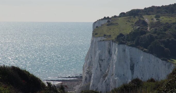 Wide Shot of the white cliffs of Dover with trees and foliage on top and the English Channel
