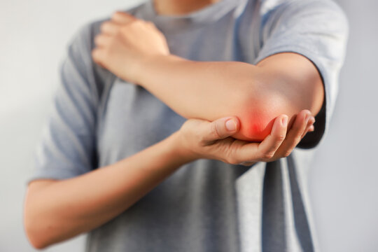 Young woman suffering from acute elbow pain and joint inflammation with red highlight effect, female touching sore arm, tendonitis, sports injury, arthritis, health problem, copy space background.