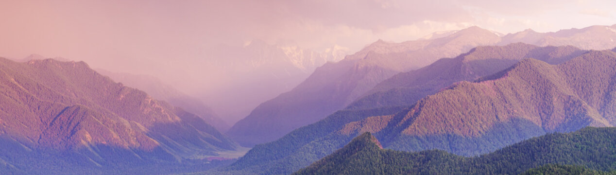 Dramatic sunset in the mountains, stormy sky, forest and peaks in the evening light, panoramic view
