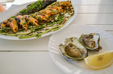 Grilled seafood platter with shrimp and fish, accompanied by fresh oysters and lemon slices on a white table.