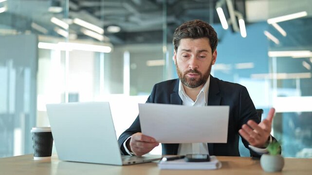 Professional appearing stressed, confused, overwhelmed while reviewing important documents. Trying to solve complex problems, using laptop at modern office workspace, reflecting work pressure.