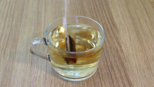 Tea bag dipping into cup of hot water and brewing tea. Close up of teabag infusing in clear glass mug on wooden table. Relaxing beverage preparation, healthy drink concept