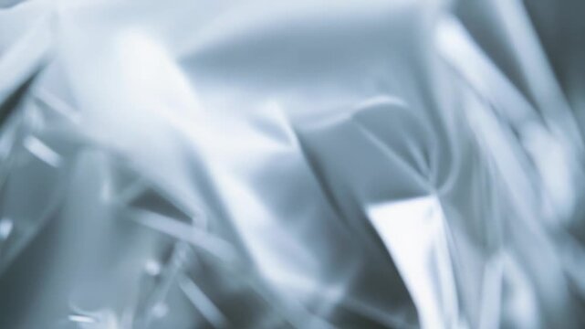 Crumpled silver foil with reflective metallic sheen and soft highlights, creating an abstract, modern textured background of waves, folds and glossy liquid like surfaces