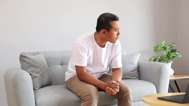 Anxiety, Asian man and nervous on sofa in home with stress, trauma or stimming with overthinking. Mental health, panic attack