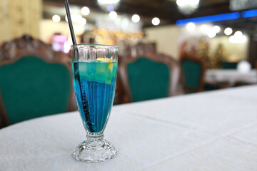 Blue cocktail with straw and ice on white table cloth