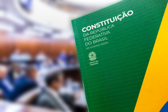 The Brazilian Federal Constitution, updated to amendment 135/2024, in focus. Municipal council plenary session is blurred in the background, symbolizing law and democracy in Brazil.