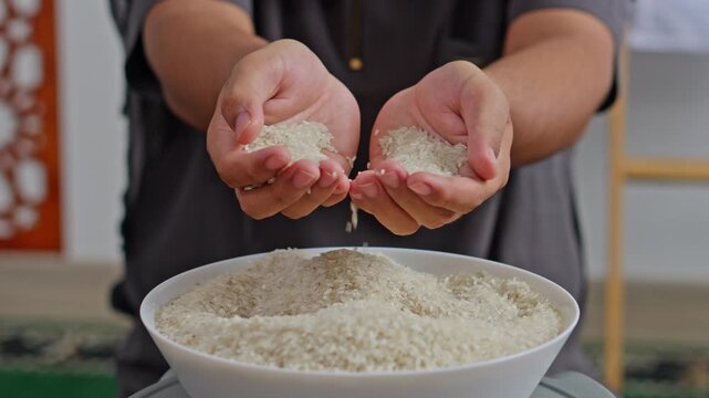 Close-up of hands releasing rice grains into bowl for Zakat al-Fitr or food charity
