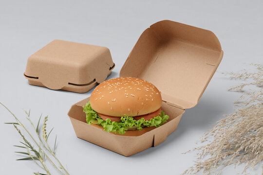 A hamburger in an open cardboard box with closed companion boxes beside it on a plain surface