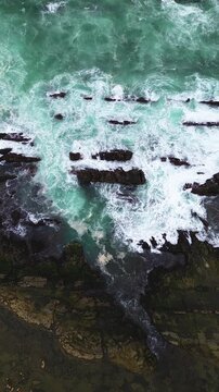 Aerial drone footage of waves breaking against sharp coastal rocks at Sawarna Beach, Banten, Indonesia. Turbulent water movement captured in clean Vertical orientation.