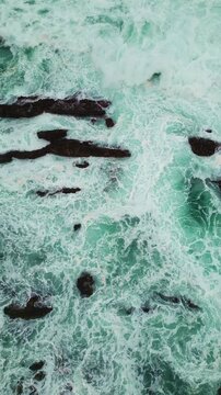 Drone top down view revealing abstract ocean textures and scattered rock formations at Sawarna Beach, Banten, Indonesia. Natural patterns and colors presented in high-resolution Vertical shot.