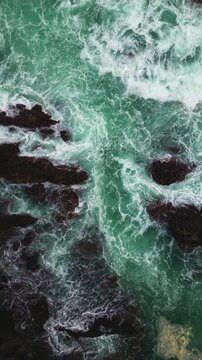 Aerial capture of ocean waves colliding with dark coastal rocks at Sawarna Beach, Banten. Strong natural contrast and movement shown in Vertical drone footage.