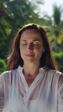 Woman meditating outdoors with eyes closed, practicing deep breathing in a serene tropical garden, vertical shot