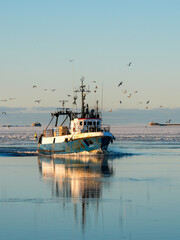 Fototapeta premium Fishing Vessel Returning to Liepaja Port Through Icy Baltic Sea at Winter Sunset