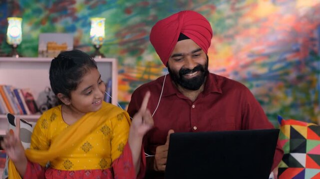 A cheerful Sikh Indian father-daughter wearing white earphones listening to music - favorite songs  playlist. A loving Indian dad and his adorable girl using a laptop together in the living room - ...