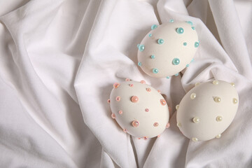 Easter eggs decorated with pearls on white fabric