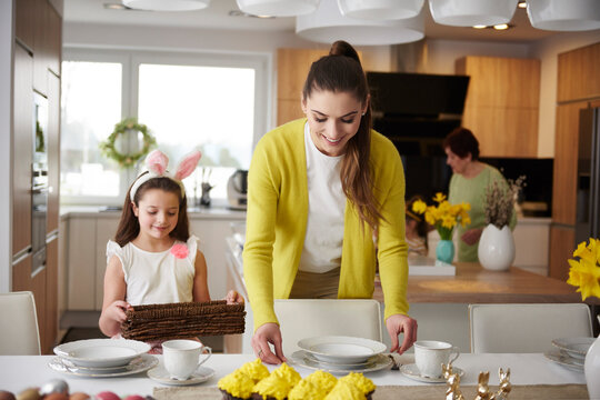 Smiling mother and daughter setting the table at home together
