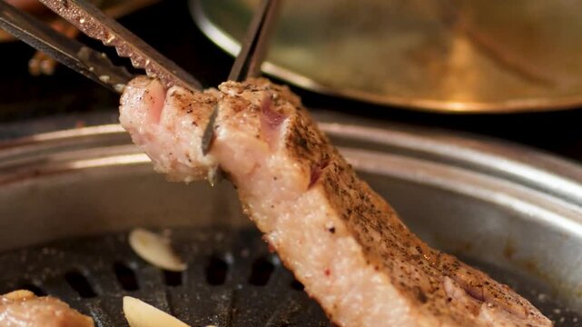 Close Up of Scissors Cutting Grilled Pork Belly on Tabletop Grill