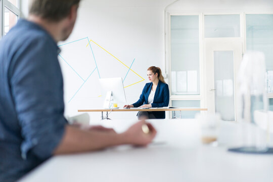 Businesswoman working in office with colleague sitting in foreground