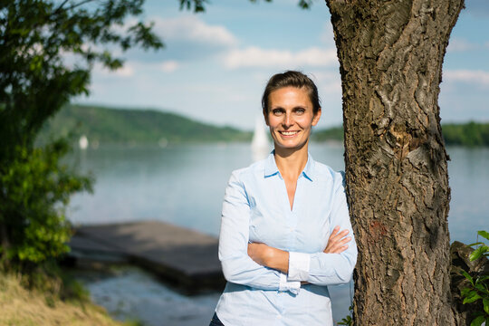 Portrait of smiling woman leaning against a tree at a lake