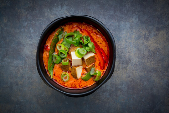 Bowl of red Thai Curry with snow peas, carrots, bell pepper, spring onions and smoked tofu
