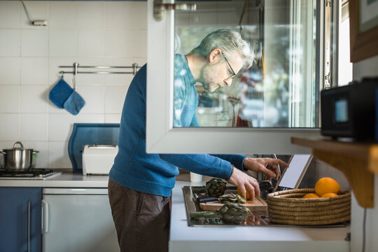 Mature man preparing artichoke in his kitchen using digital tablet