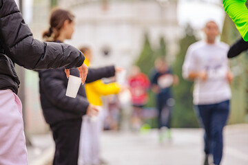 Fototapeta premium Volunteer offers a plastic cup of water to marathon runners