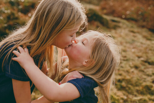 Two cute blond sisters kissing outdoors