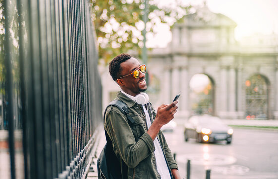 Smiling man wearing sunglasses using smart phone while standing in city