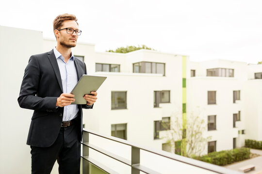 Businessman with tablet standing on balcony in a development area