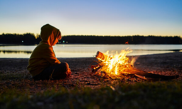 Argentina, Patagonia, Concordia, boy sitting at camp fire at a lake
