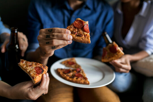 Close-up of tattooed man with friends holding pizza slice