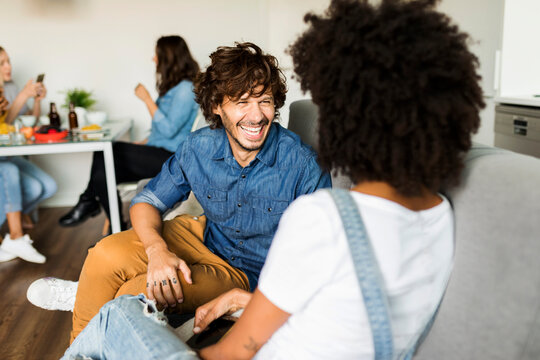 Happy couple sitting on couch talking with friends in background