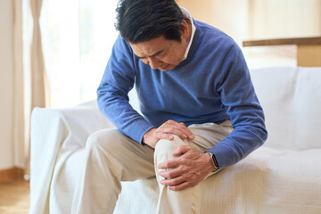 痛む膝を押さえるアジア人シニア男性
