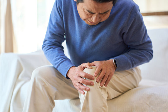 痛む膝を押さえるアジア人シニア男性