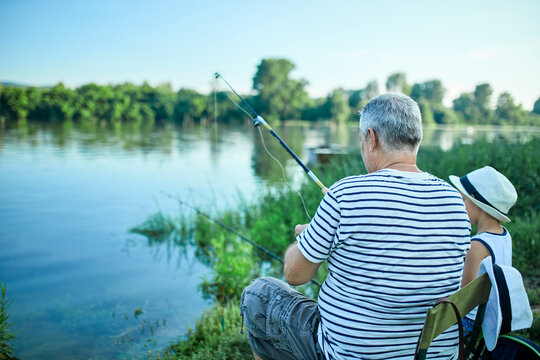 Back view of grandfather and grandson fishing together at lakeshore