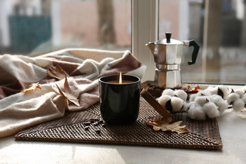 Burning candle, coffee beans and autumn leaves on windowsill in living room, closeup