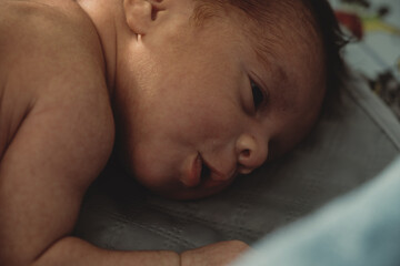 Close up of newborn lying on side on soft surface. Intimate image conveying calmness, delicacy and early neonatal stage at home.
