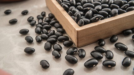Black beans in a square container and black beans scattered on the table.