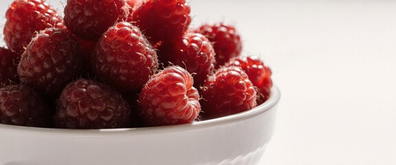 Fresh raspberries piled high in a white bowl, bathed in soft natural light
