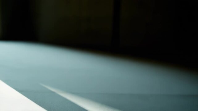Sunlight casting strong linear shadows across a lightly textured, pale surface, creating a dynamic contrast between illuminated areas and deep, geometric patterns