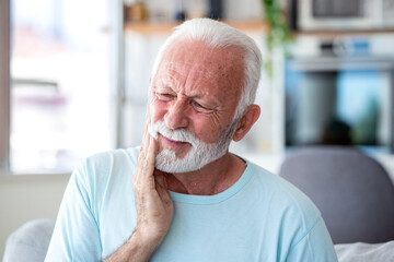 Obraz premium Senior man with toothache touching his face. Elderly male patient suffering from dental pain or sensitive teeth at home. Healthcare and medicine concept. Old person with gingivitis or oral problem.