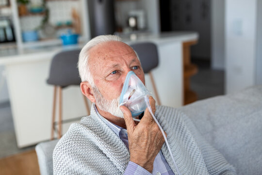 Senior man using oxygen mask at home. Elderly male patient with respiratory problems breathing through nebulizer. Healthcare, asthma, and COPD treatment concept. Retired man with medical equipment.