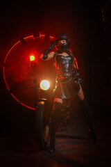 Fototapeta na wymiar Stylish beautiful young woman in black leather corset and boots posing on vintage motorcycle on old garage dark interior background.