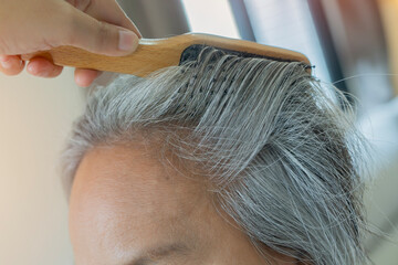 Naklejka premium Asian mature woman with gray hair and combing her hair at home.