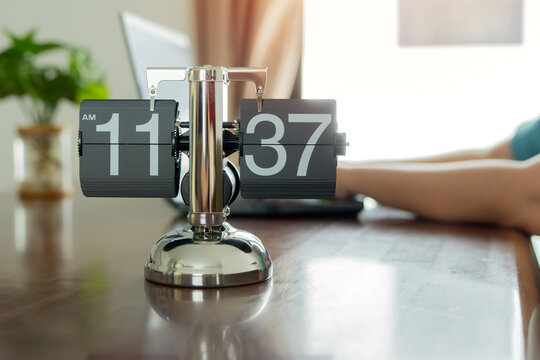 Vintage flip clock on table in office with blurred background of woman work with laptop.