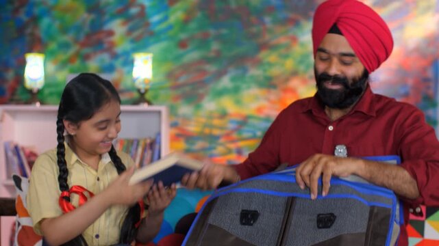 A handsome Sikh Indian guy happily packing his daughter's bag pack for her school - parent-child bonding
. An adorable girl child in school uniform and a caring Indian father together in the livin...