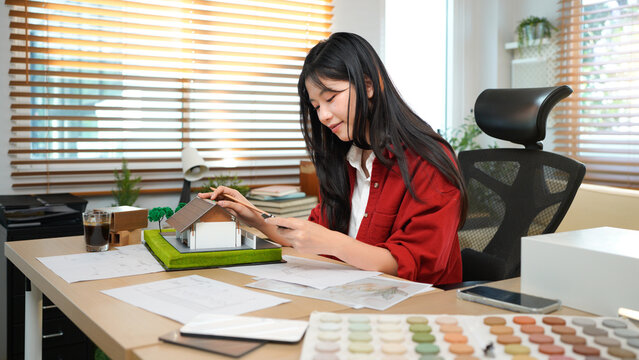 Expert asian architect woman doing house model by wooden plank at home office. Asian decorator woman design and choosing material make model structure for presentation to customer in office.